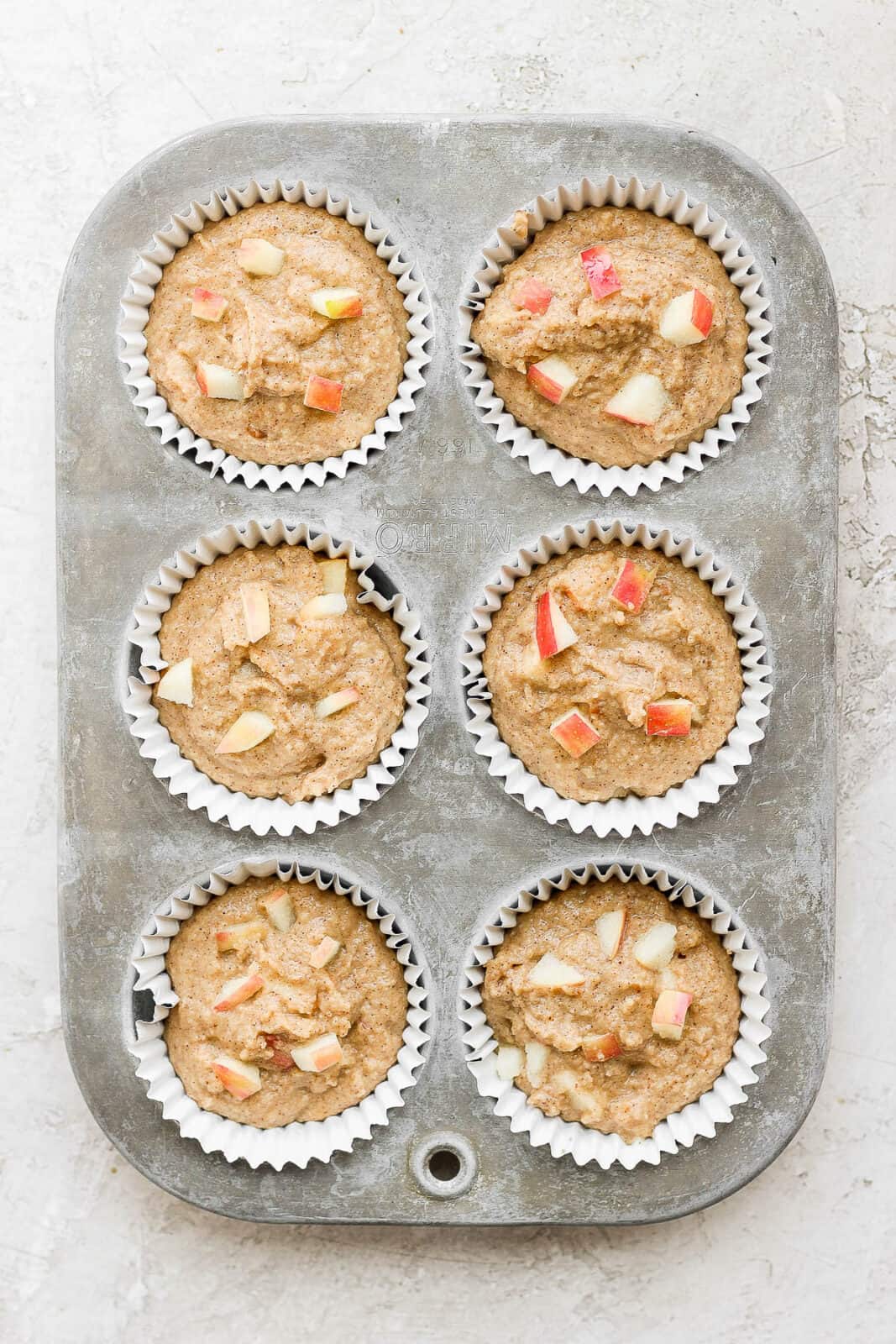 Batter for apple cinnamon muffins in a muffin tin before baking.