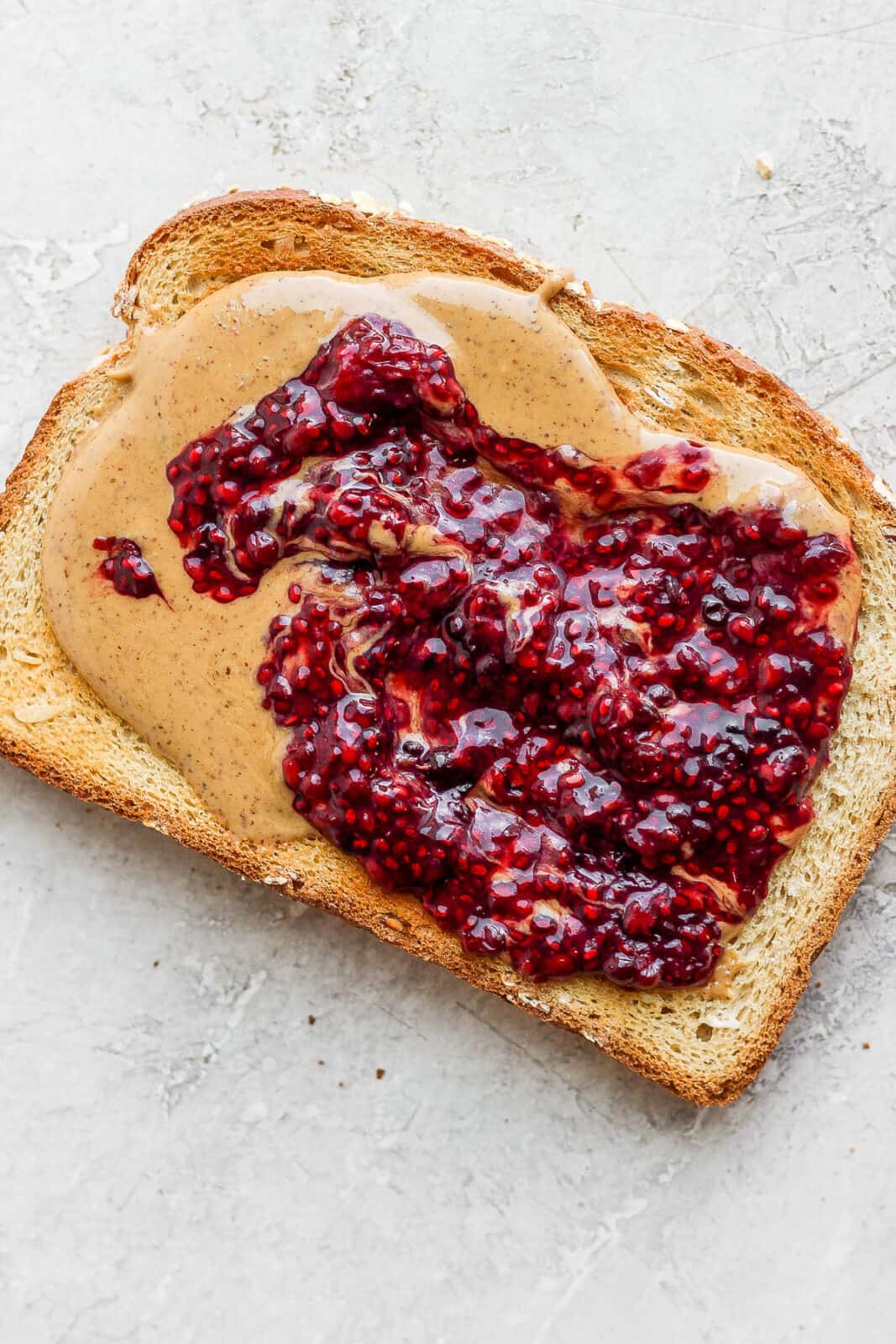 A piece of toast with almond butter and homemade chia sed jam spread on it. 