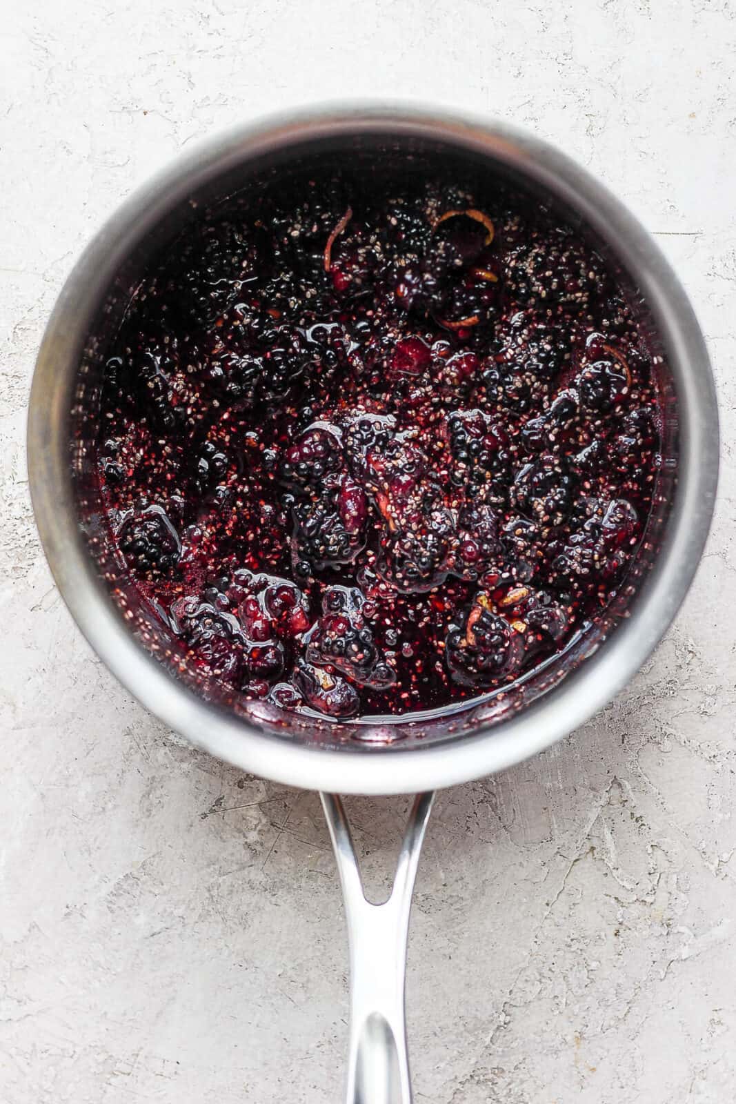 A saucepan with mashed blackberries, lemon zest and other ingredients for chia jam. 