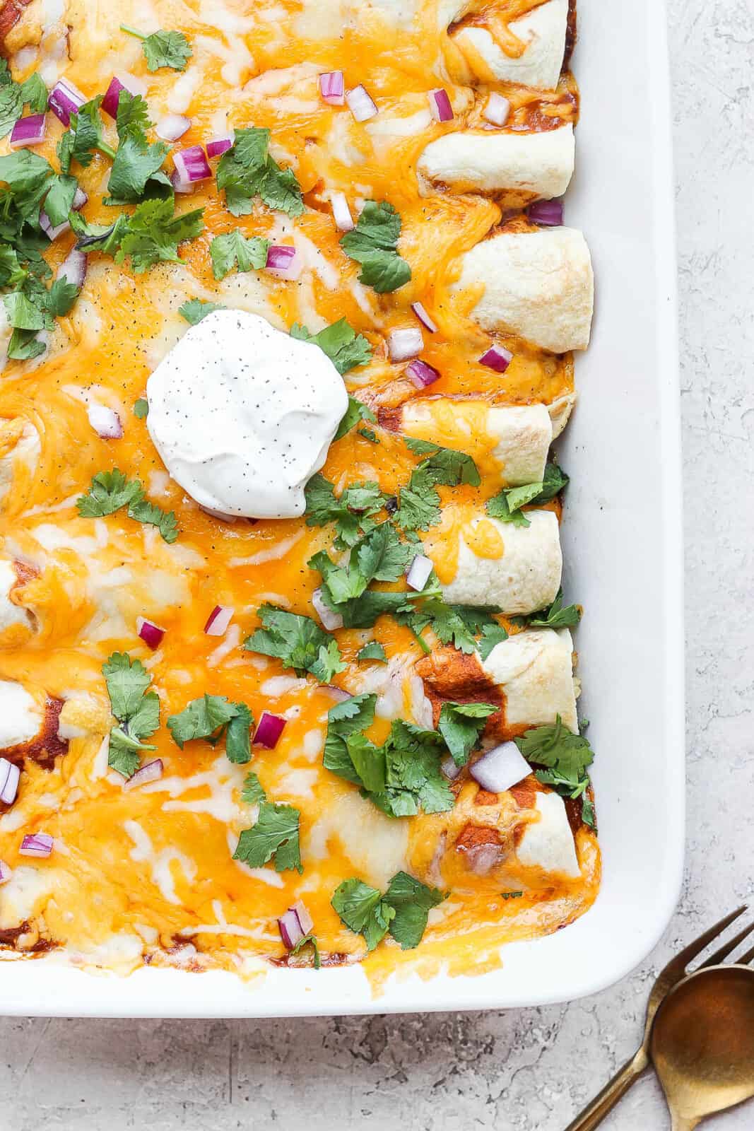 A pan of healthy chicken enchiladas with some sour cream on top. 