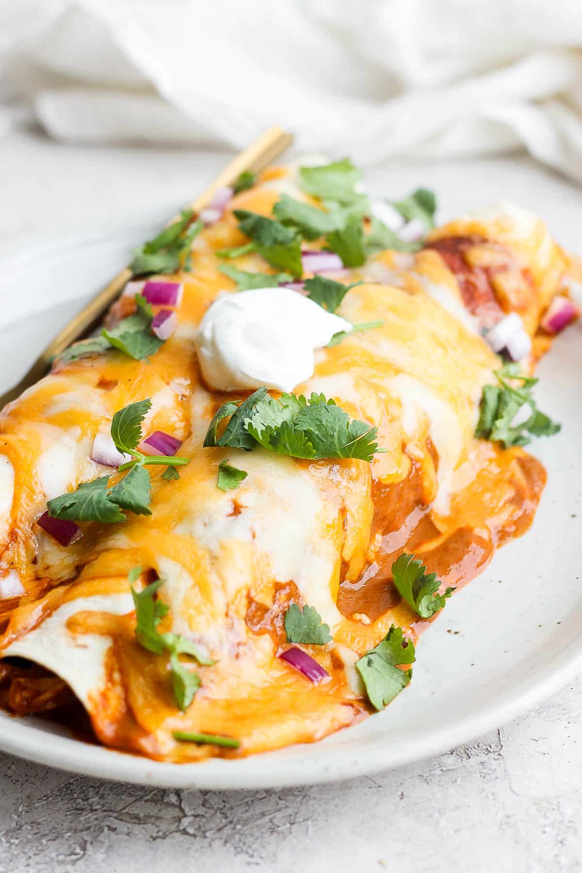 Two chicken enchiladas on a plate with cheese melting down the side. 