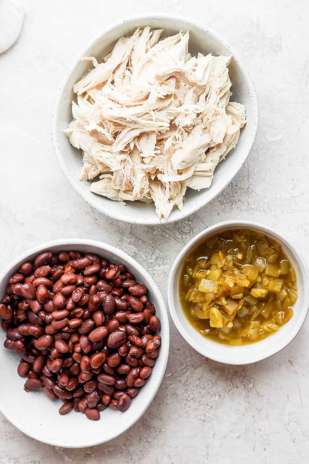 Three bowls with shredded chicken, green chiles and black beans in each. 