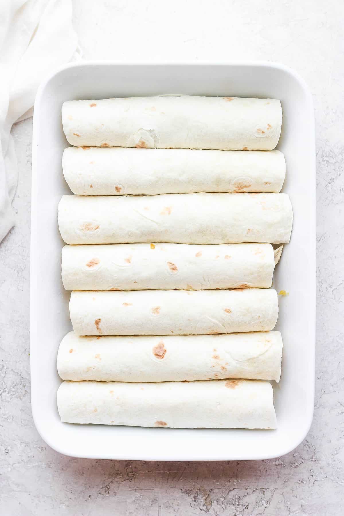 Rolled up chicken enchiladas in a pan before sauce and cheese are added.