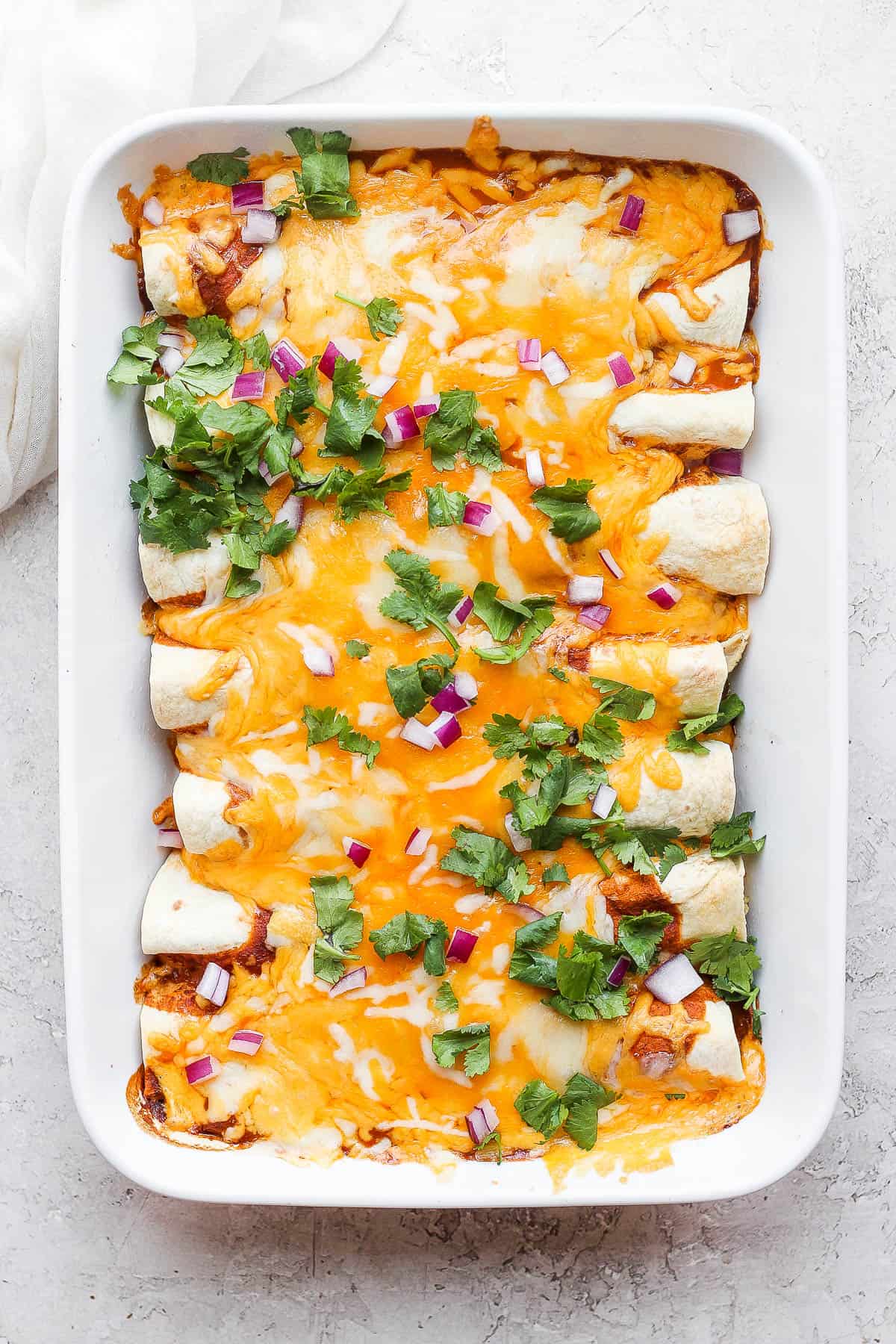 A pan of healthy chicken enchiladas with cilantro and red onion on top. 