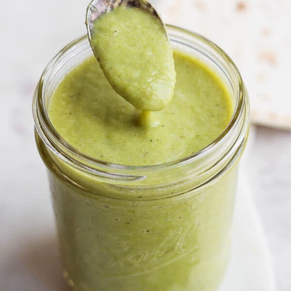 Jar of green enchilada sauce with someone spooning out a little bit.