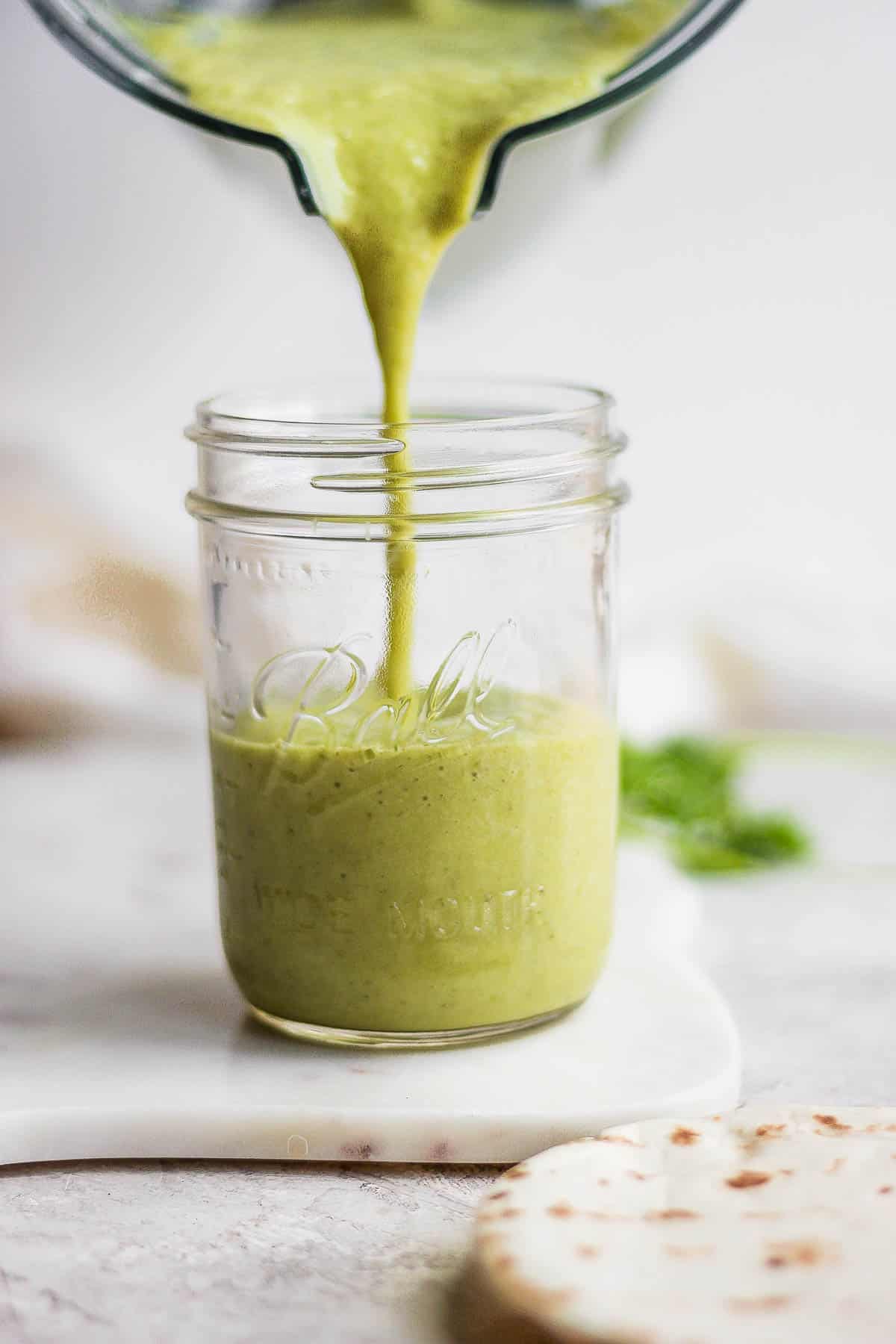 Green enchilada sauce being poured from a blender into a mason jar.