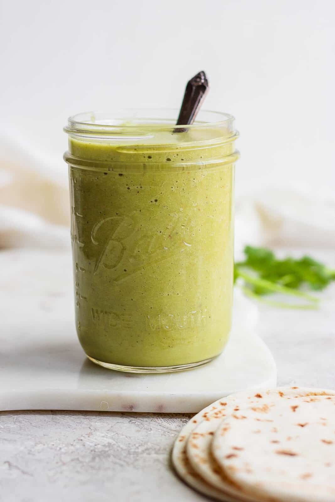 Green enchilada sauce in a mason jar with a spoon.