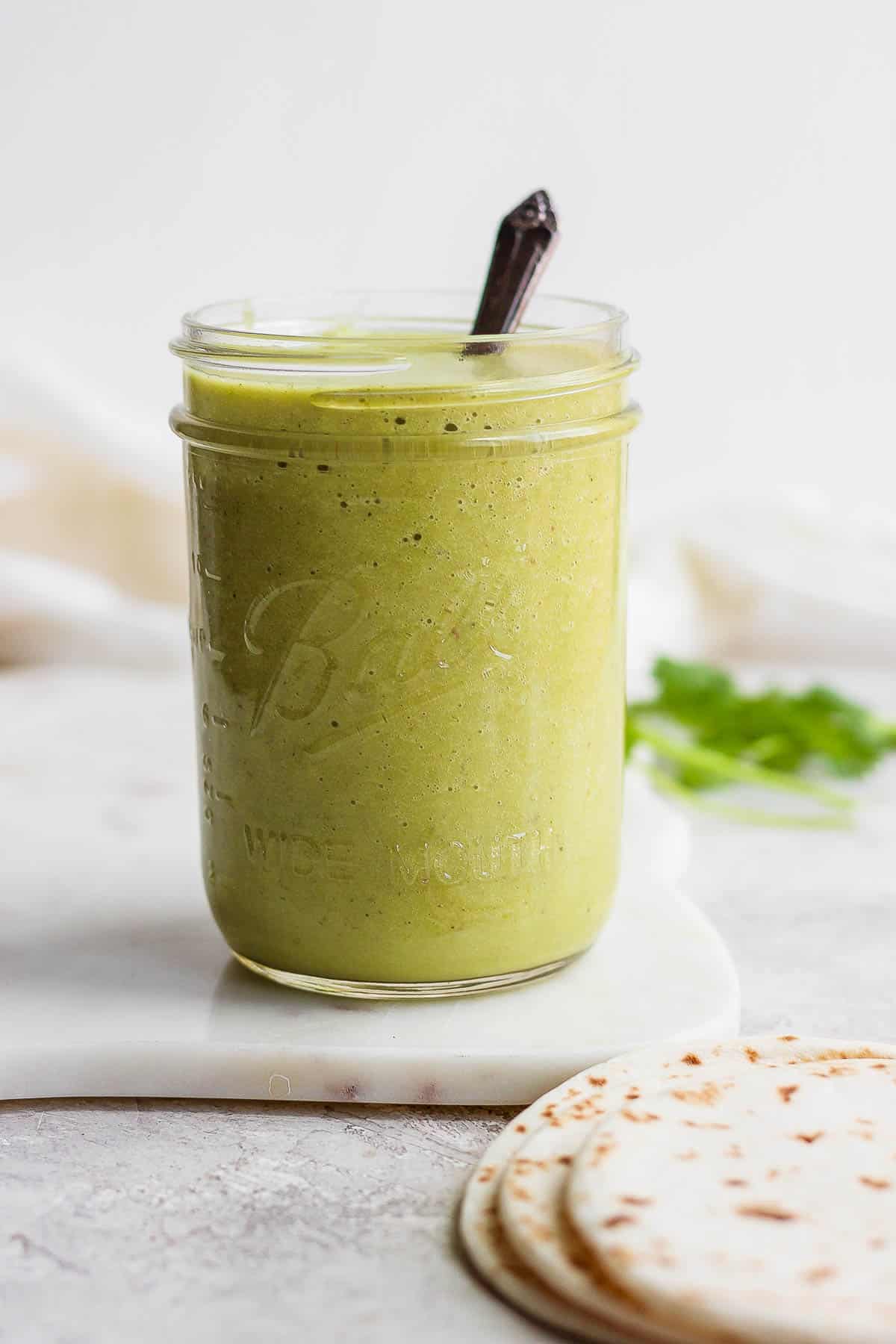 Green enchilada sauce in a mason jar with a spoon.