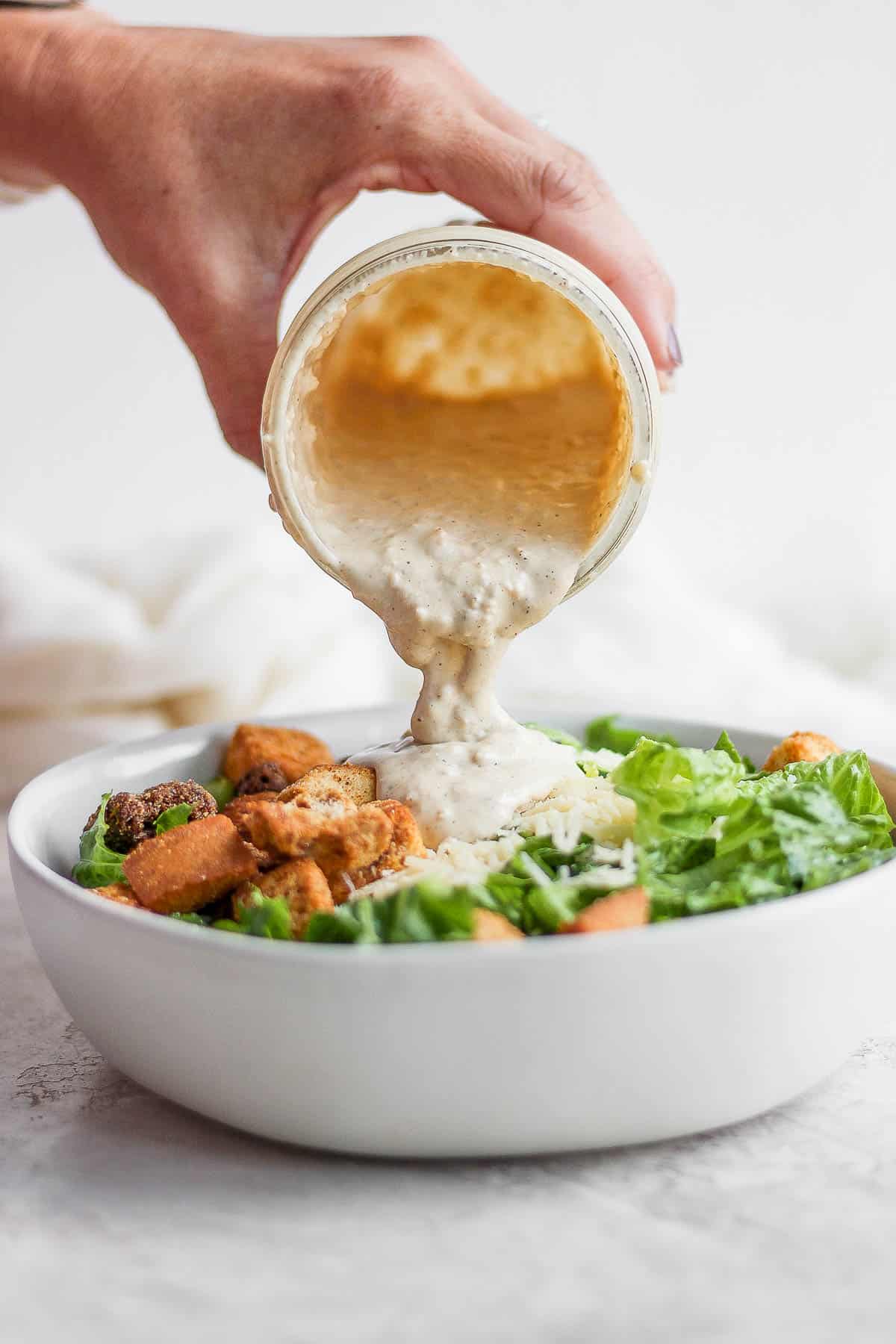 Healthy caesar dressing being poured on a salad.