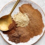 Spices for pumpkin pie spice separated on a plate with a gold spoon.