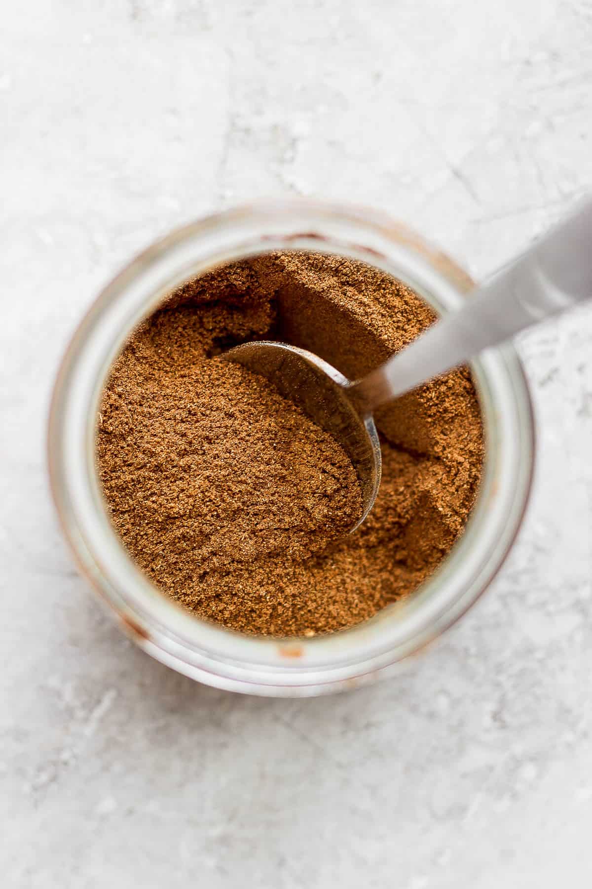 Pumpkin spice ingredients mixed together in a jar with a spoon.