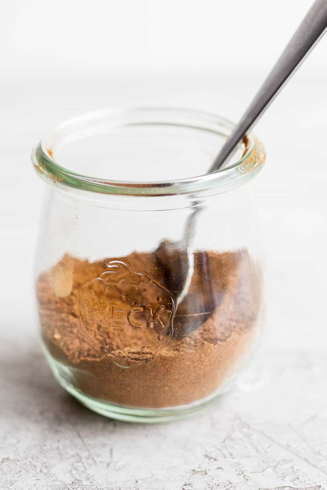 Homemade pumpkin spice ingredients in a jar with a spoon.