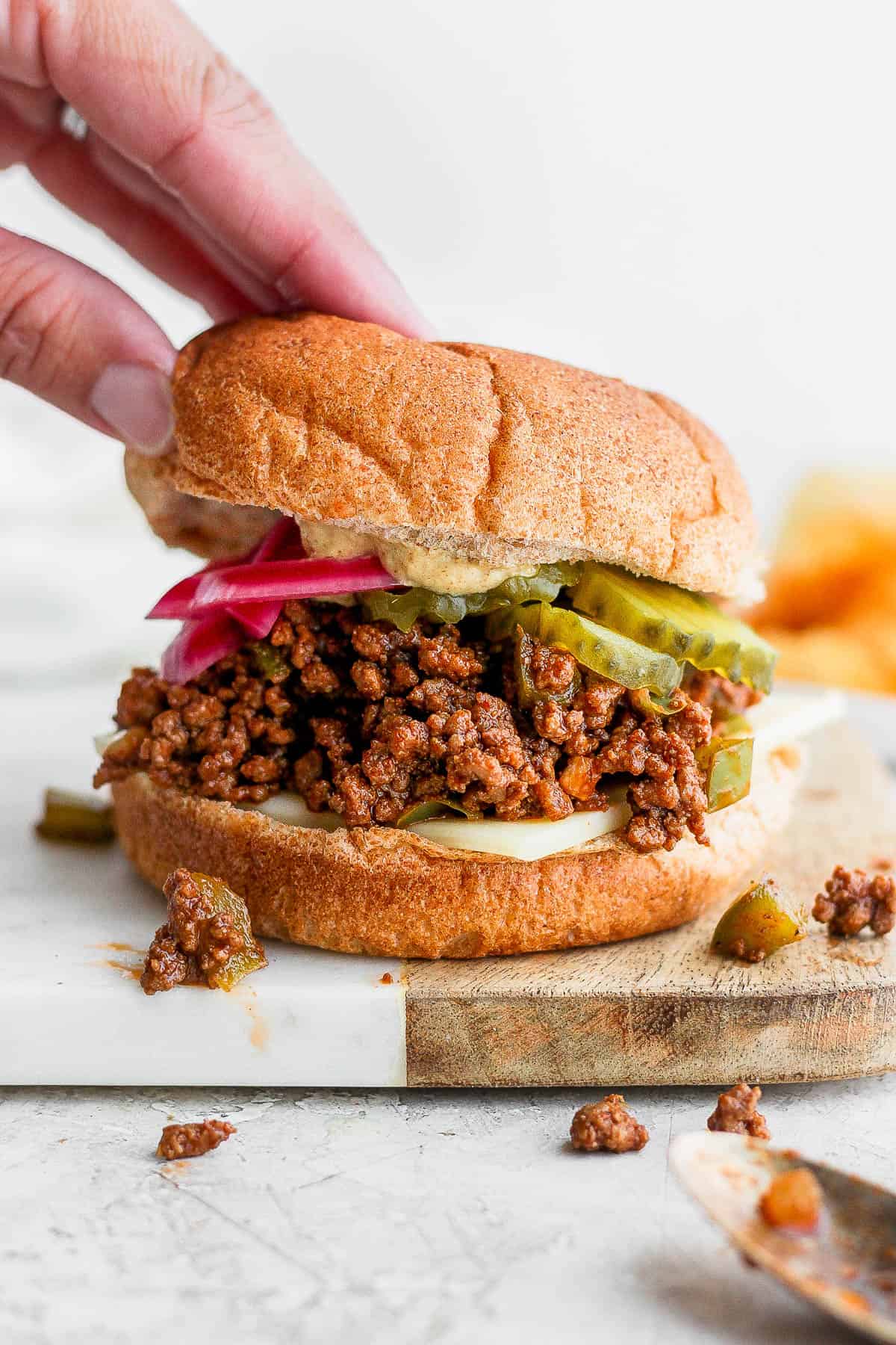 Someone setting a bun on top of a sloppy Joe sandwich. 