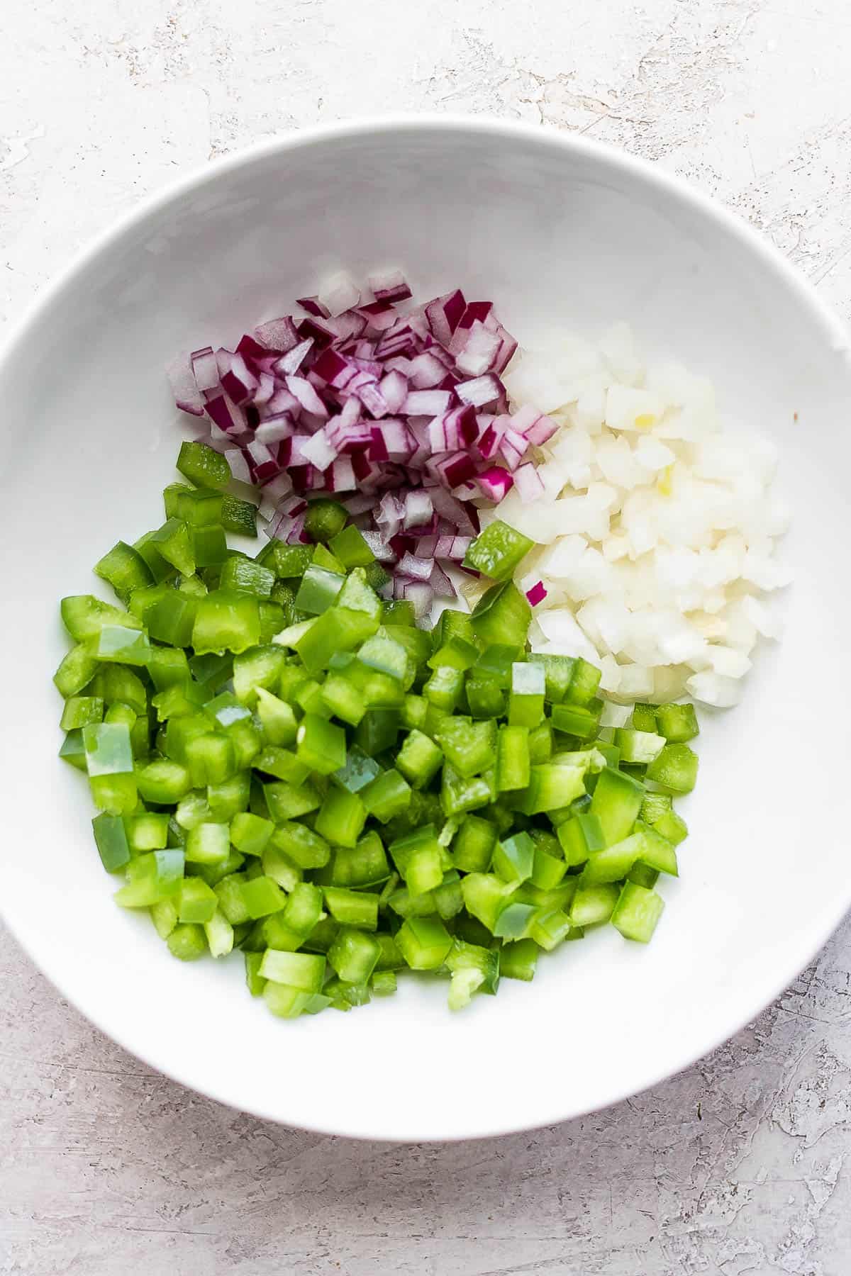 A bowl of chopped green bell pepper, yellow onions and red onions.