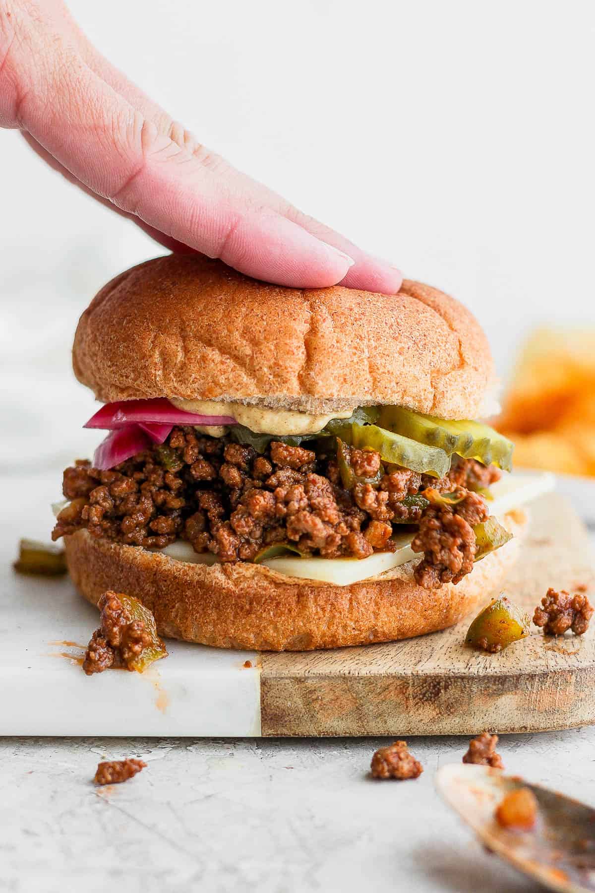 A homemade healthy sloppy Joe with someone pushing down on the top bun. 
