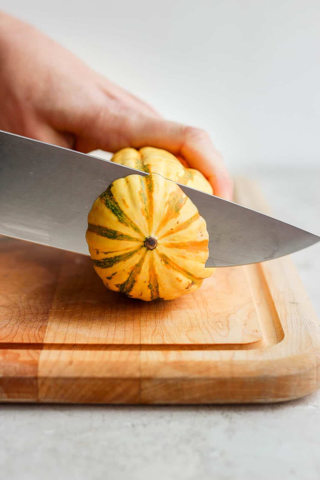 A knife cutting the end off a delicata squash.
