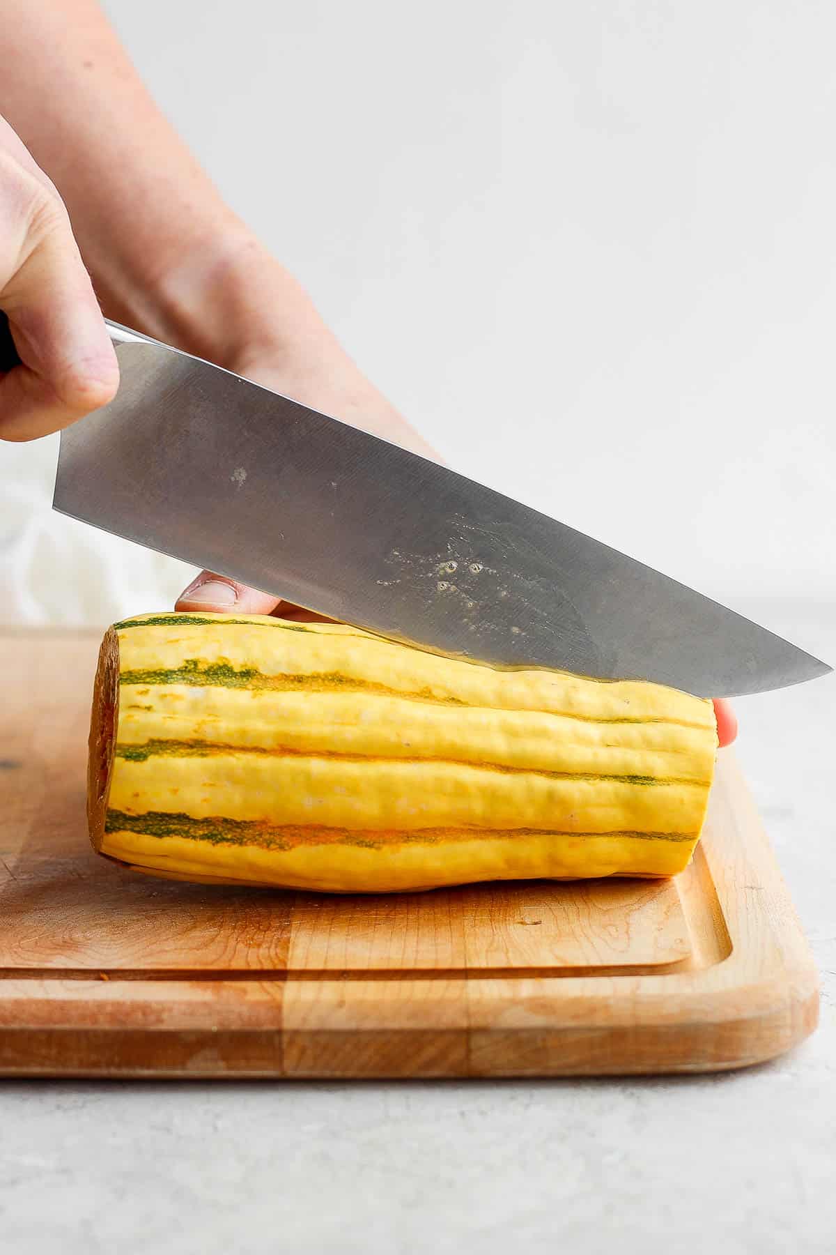 A knife cutting the delicata squash in half, length-wise.