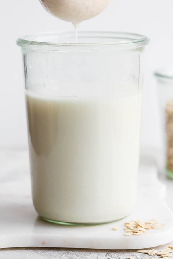 Oat milk being squeezed into a tall glass with a glass of oats in the background.