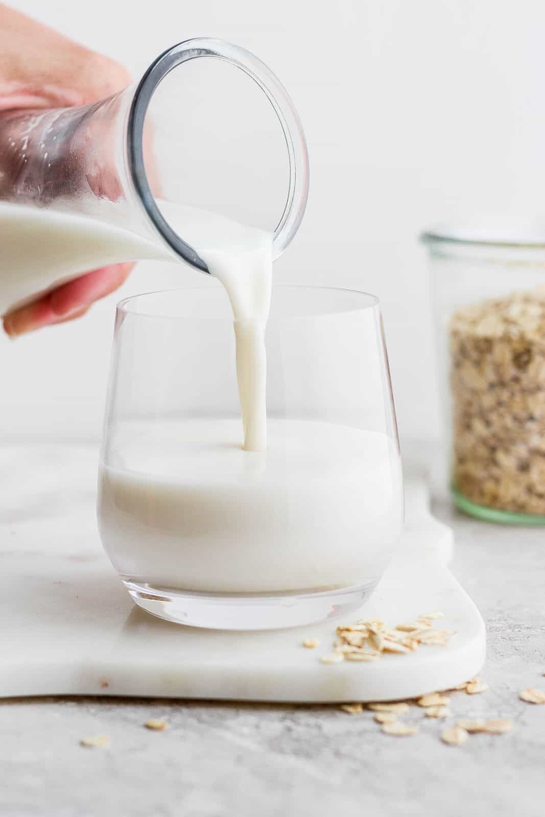 Pouring oat milk from a carafe into a glass.