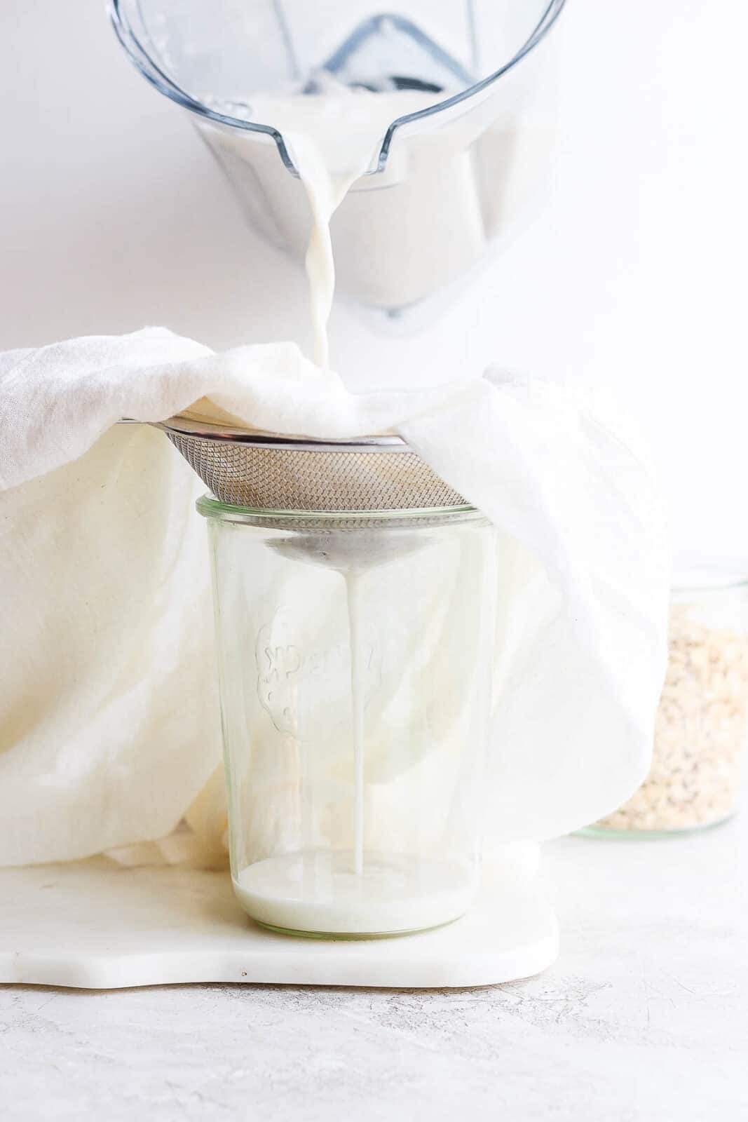 Pouring oat milk from the blender, through a cheesecloth, and into a mason jar.