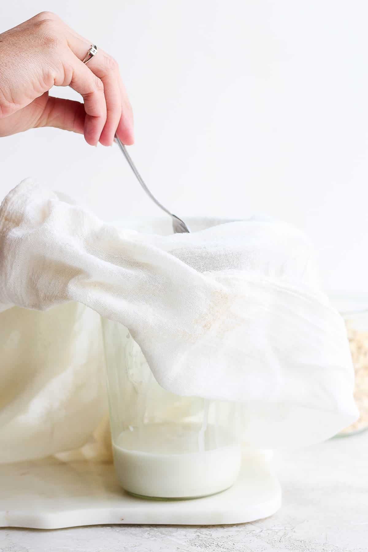 Using a spoon to move oat residue in the cheesecloth so the oat milk can run through.