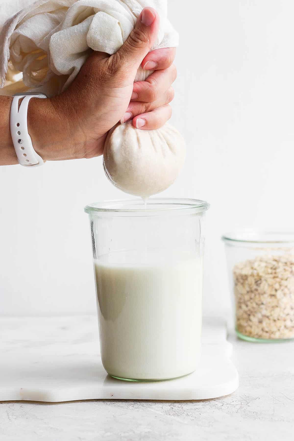 Squeezing the oat milk from the cheesecloth into the mason jar.