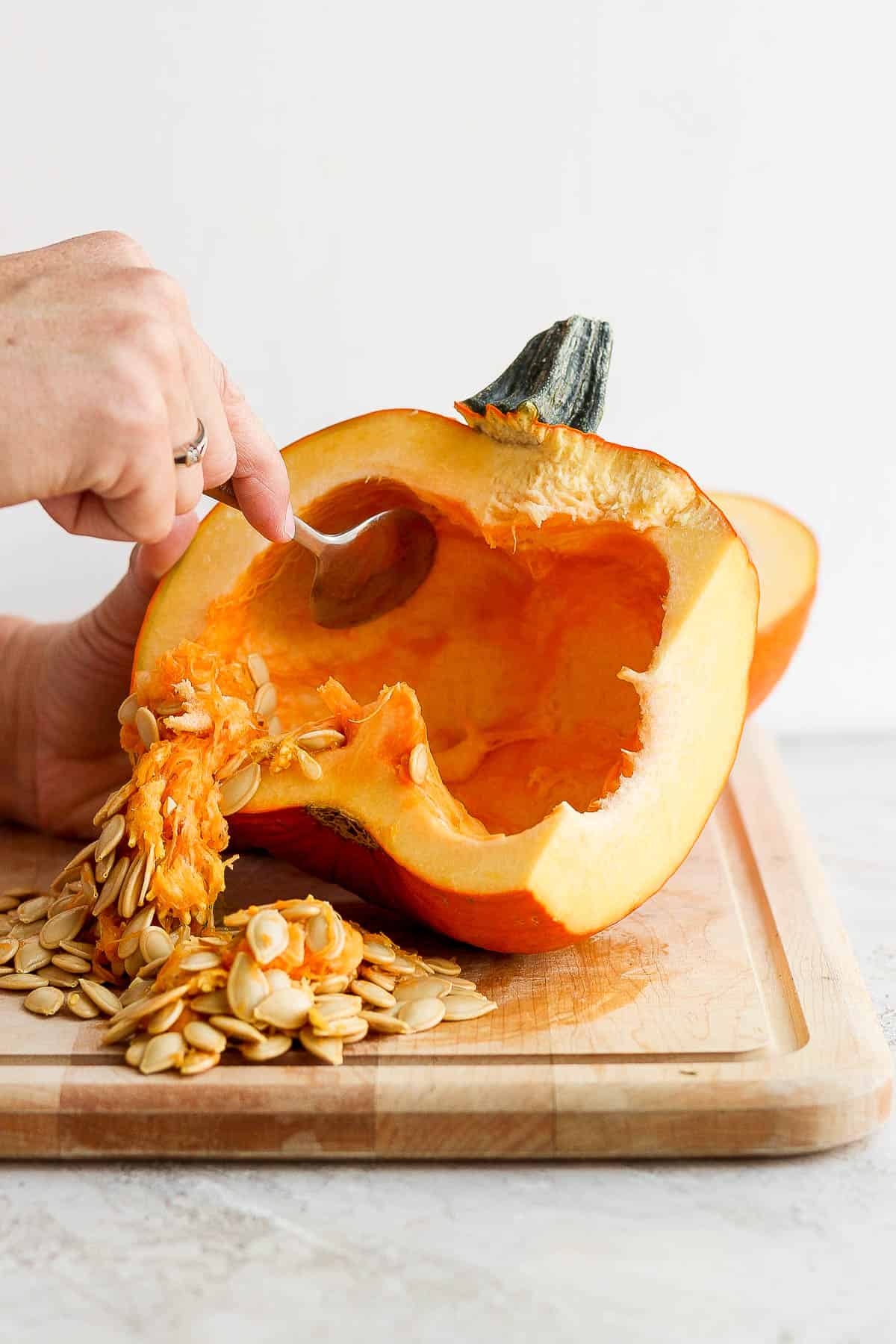 A spoon scooping the seeds and strings out of the pumpkin.