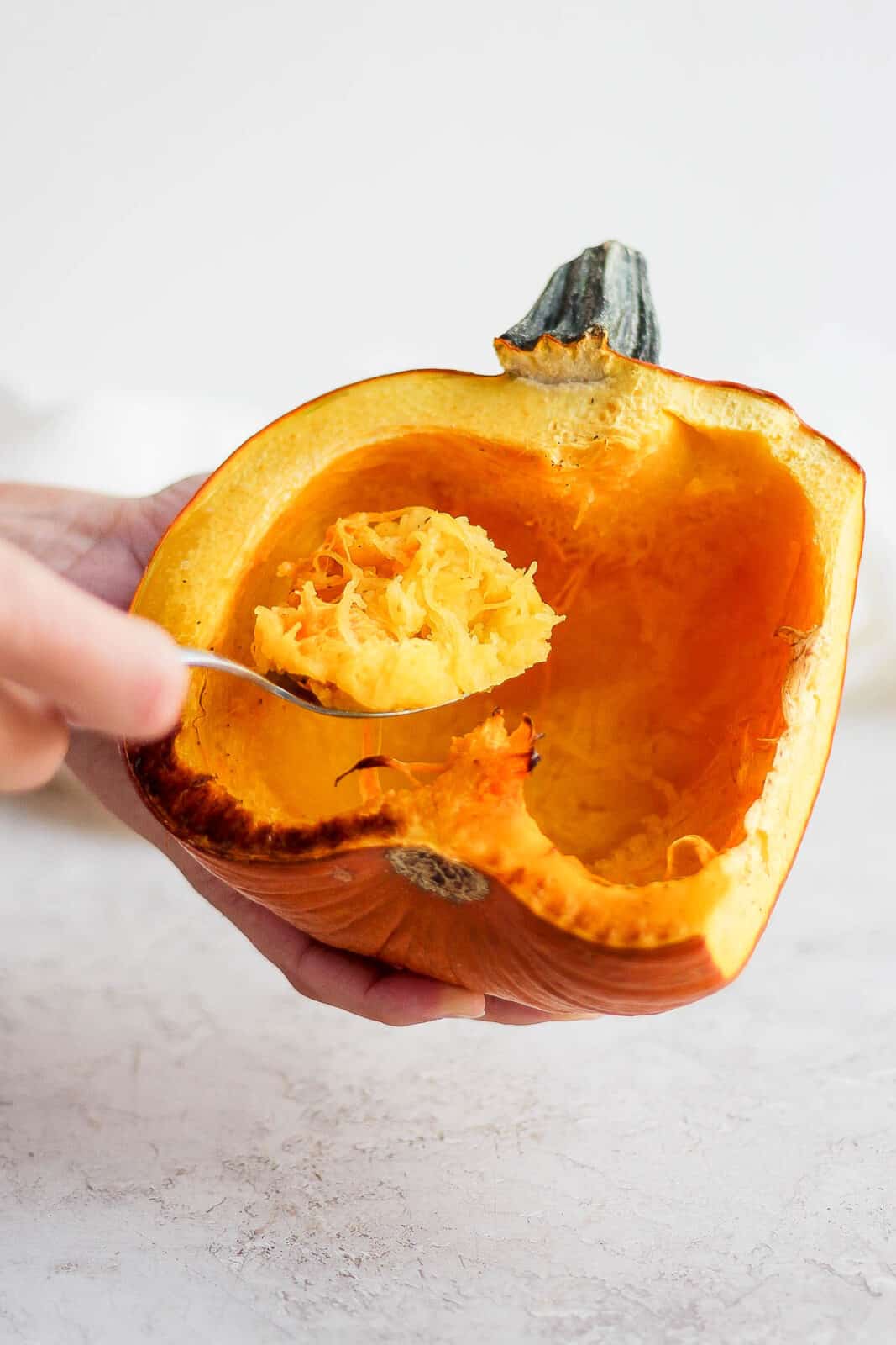 A spoon scooping the cooked pumpkin out of the shell.