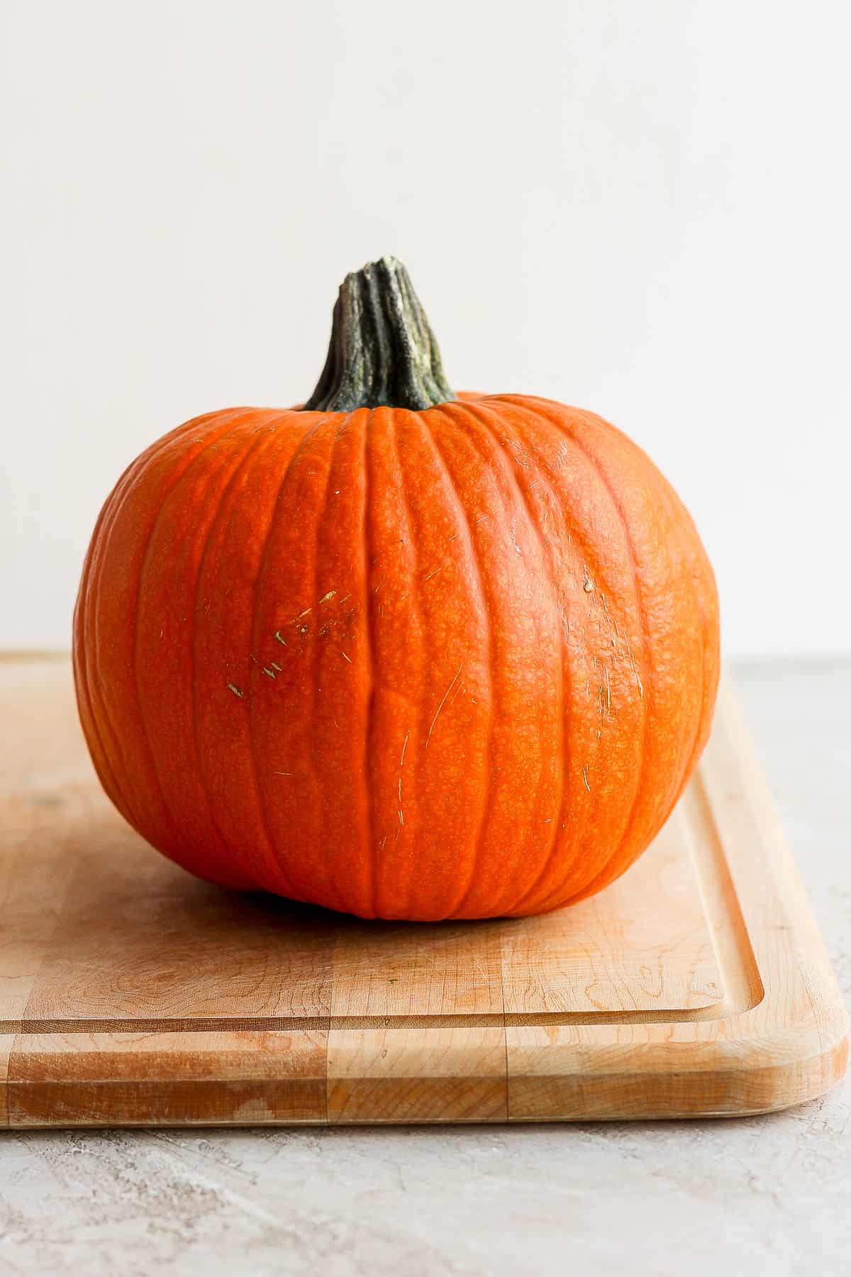 A small, baking pumpkin on a cutting board.