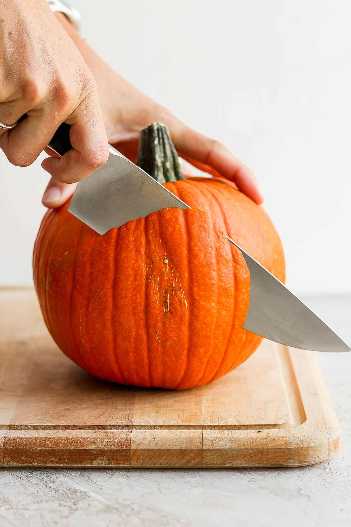 A sharp knife cutting a thin slice off the side of a pumpkin.