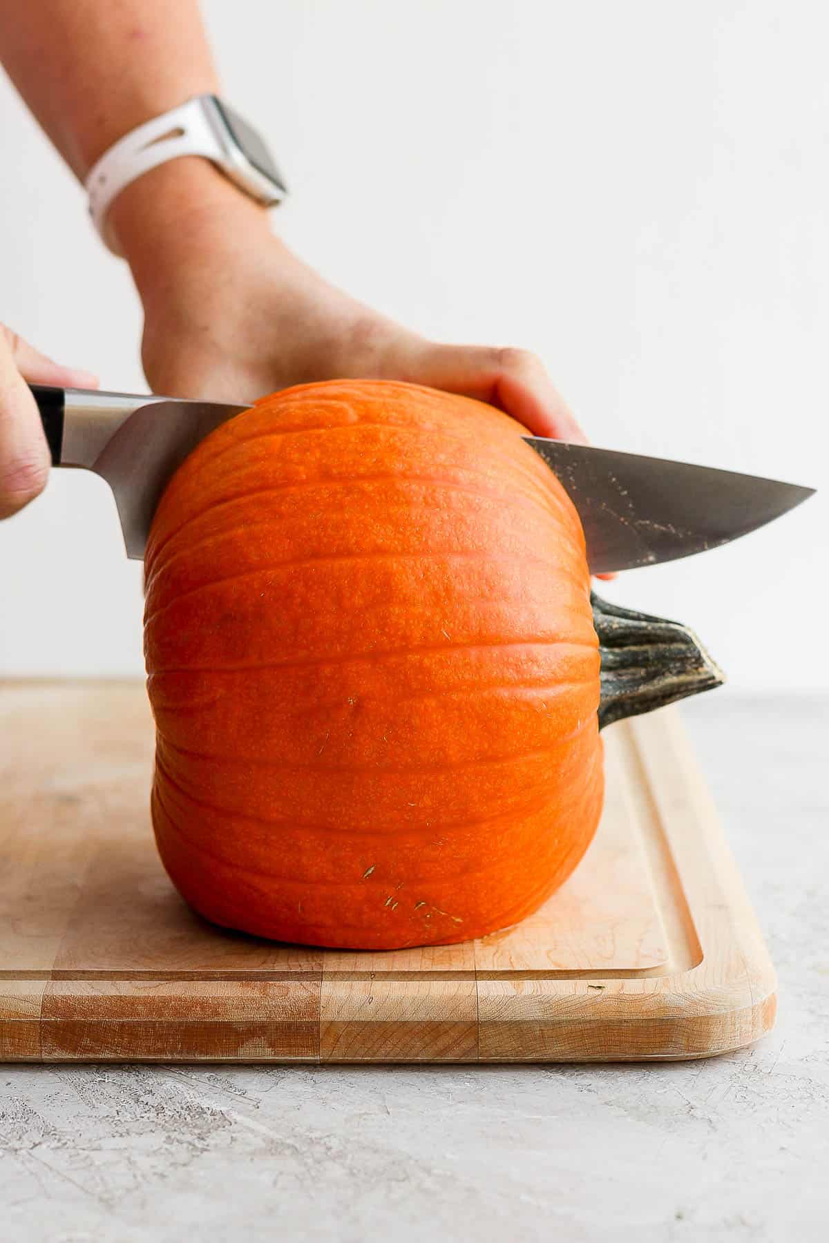A baking pumpkin being cut in half lengthwise.