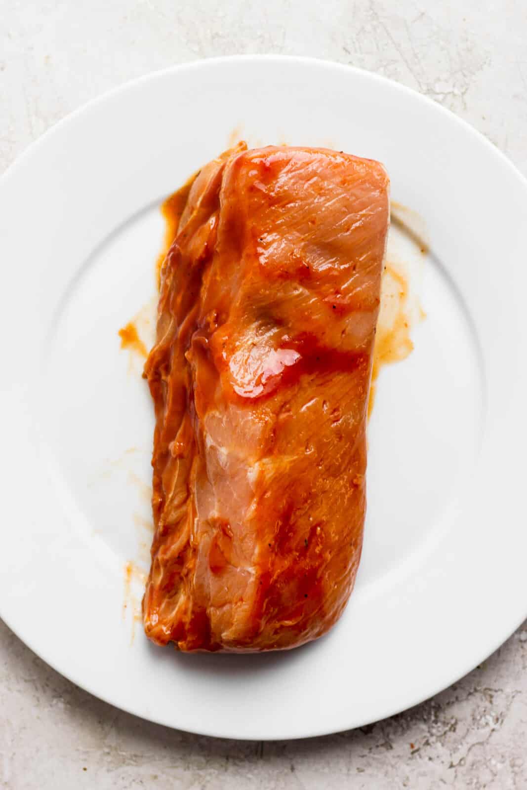 A pork loin on a plate, marinated and ready to be cooked. 