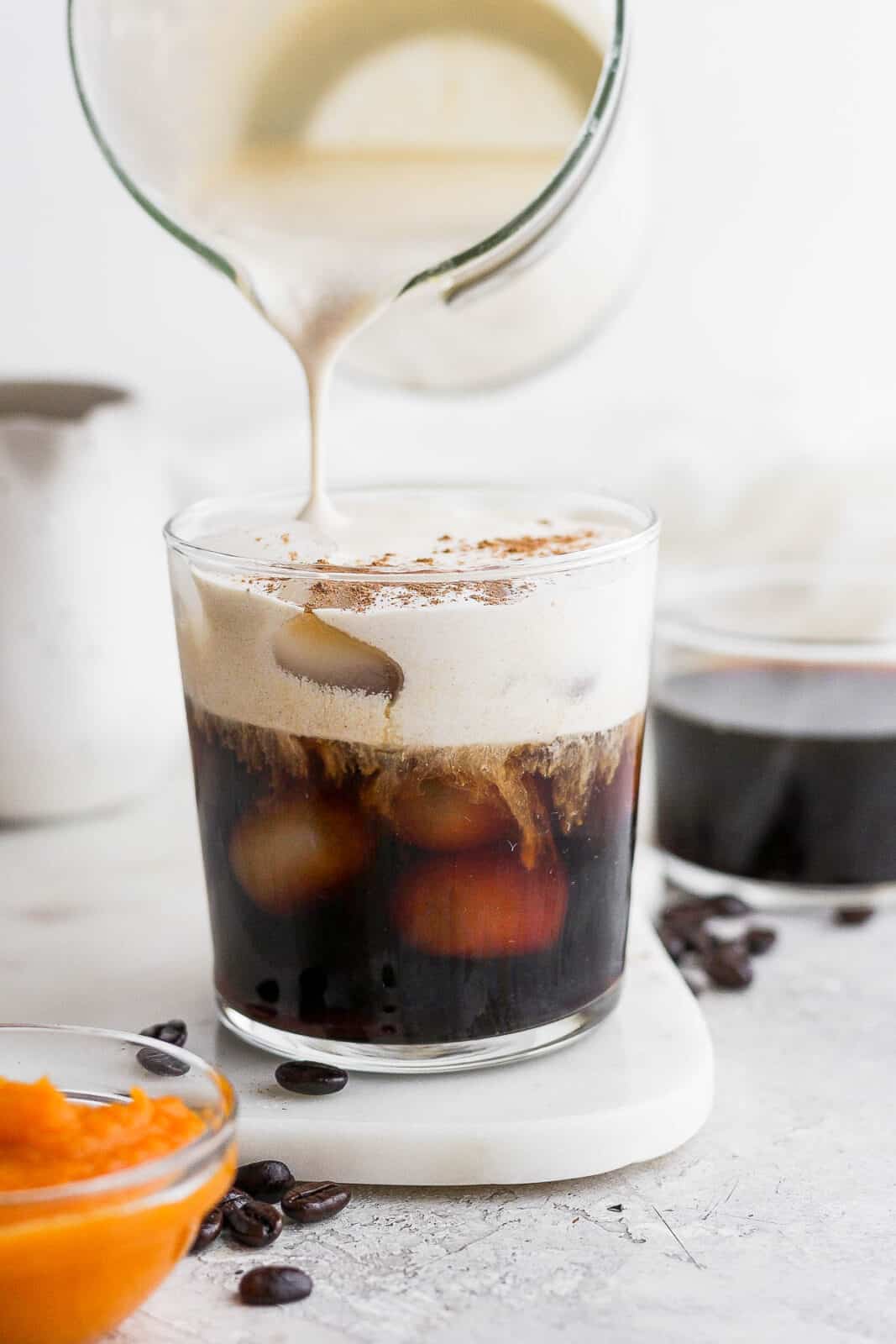 Someone pouring pumpkin cream over a glass of cold brew coffee.