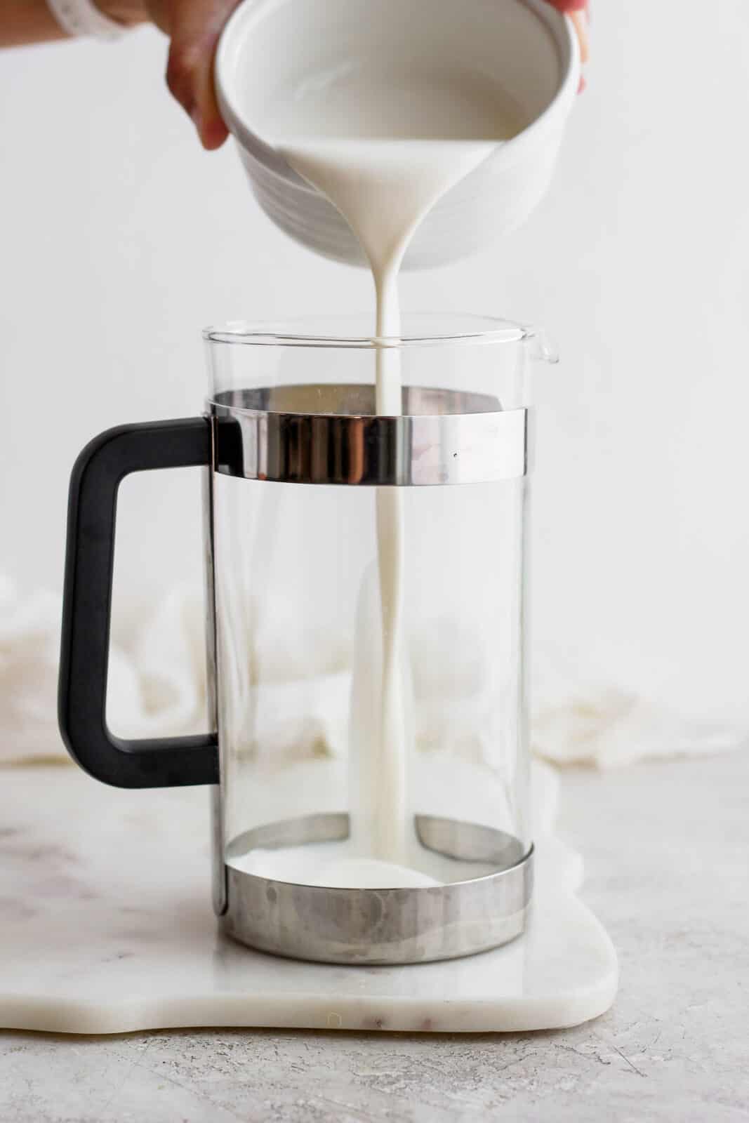 Someone pouring cream into a French press.