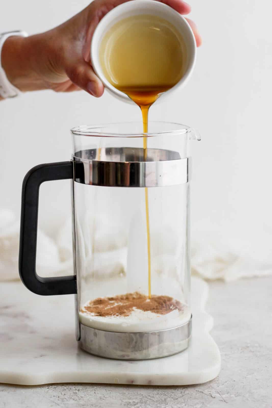 Someone pouring maple syrup into a French press.