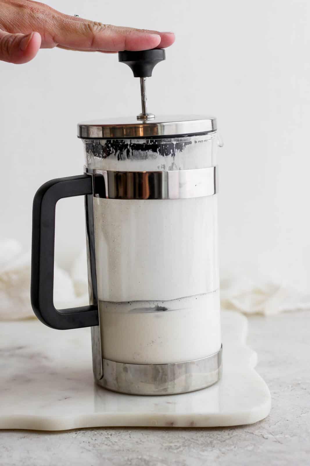 Someones pressing down on a french press to create cold foam.