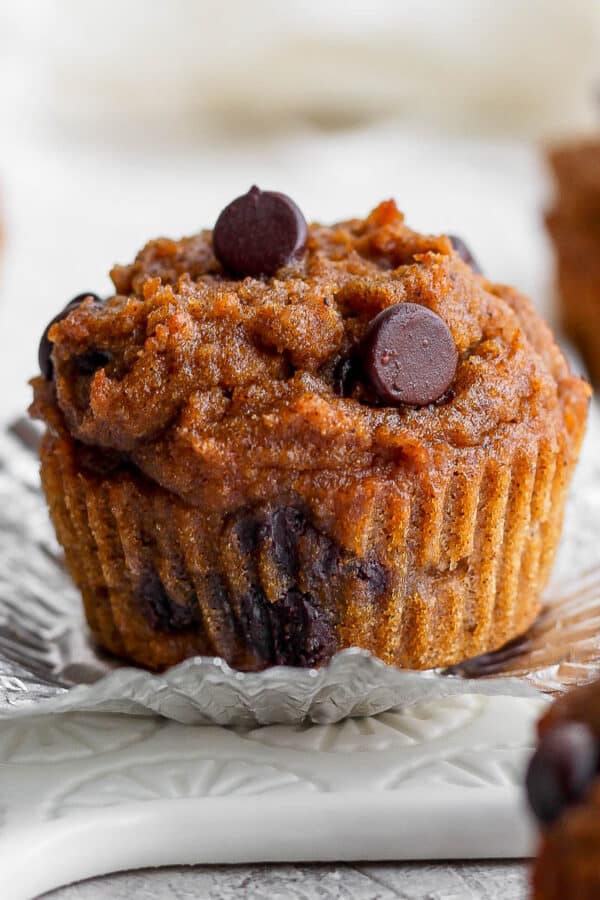 The wrapper pulled down from a pumpkin muffin with other muffins in the background.
