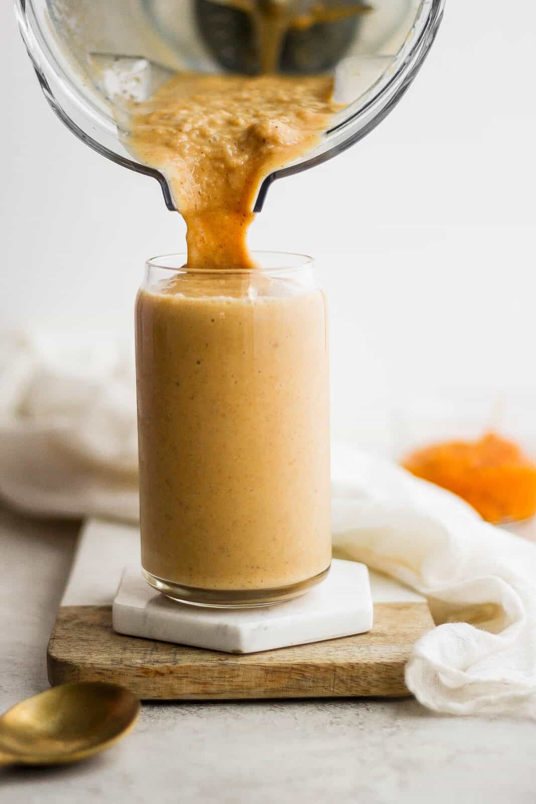 Pumpkin smoothie being poured from a blender into a glass.