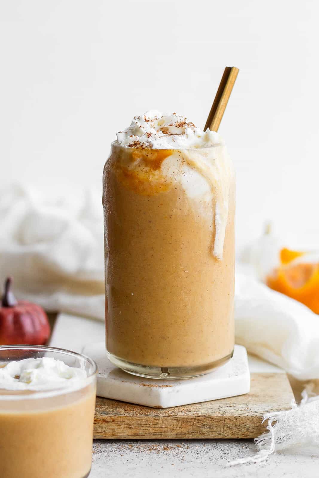 Pumpkin smoothie in a glass with whipped cream on top.
