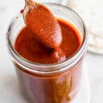 Jar of red enchilada sauce with a spoon scooping some out.