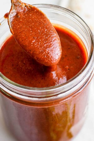 Jar of red enchilada sauce with a spoon scooping some out.