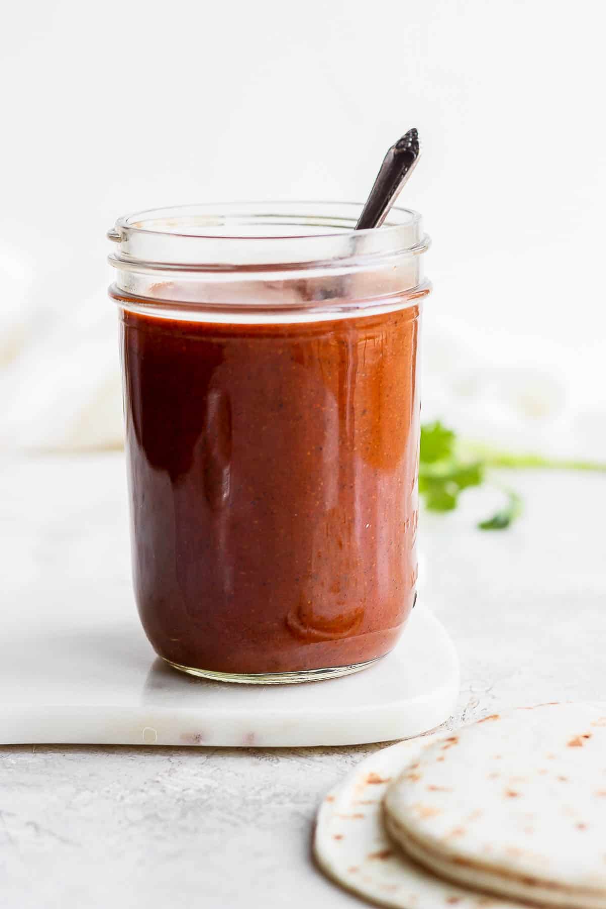Red enchilada sauce in a mason jar with a spoon.