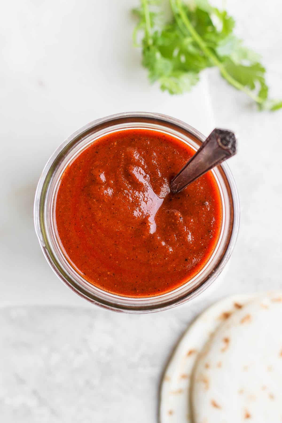 Red enchilada sauce in a jar with a spoon.