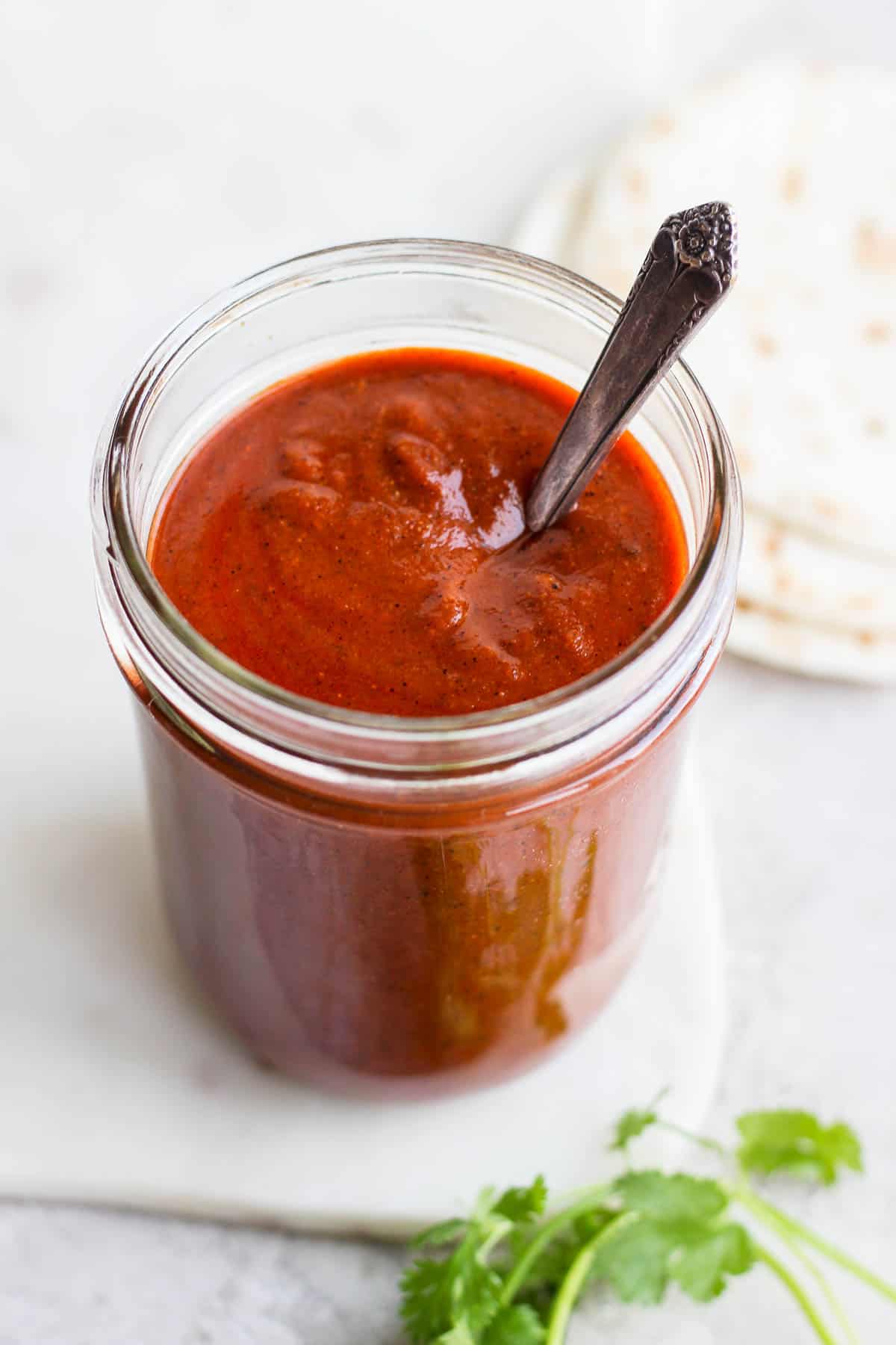 Red enchilada sauce in a mason jar with a spoon.