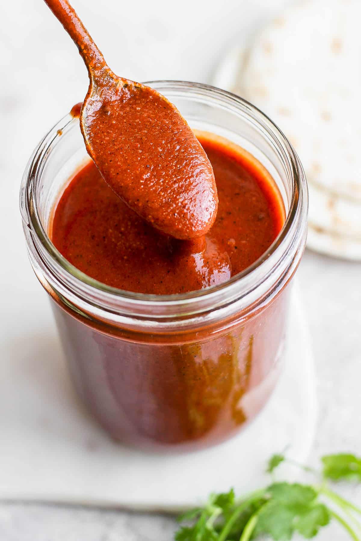A spoon coming out of the jar with red enchilada sauce.
