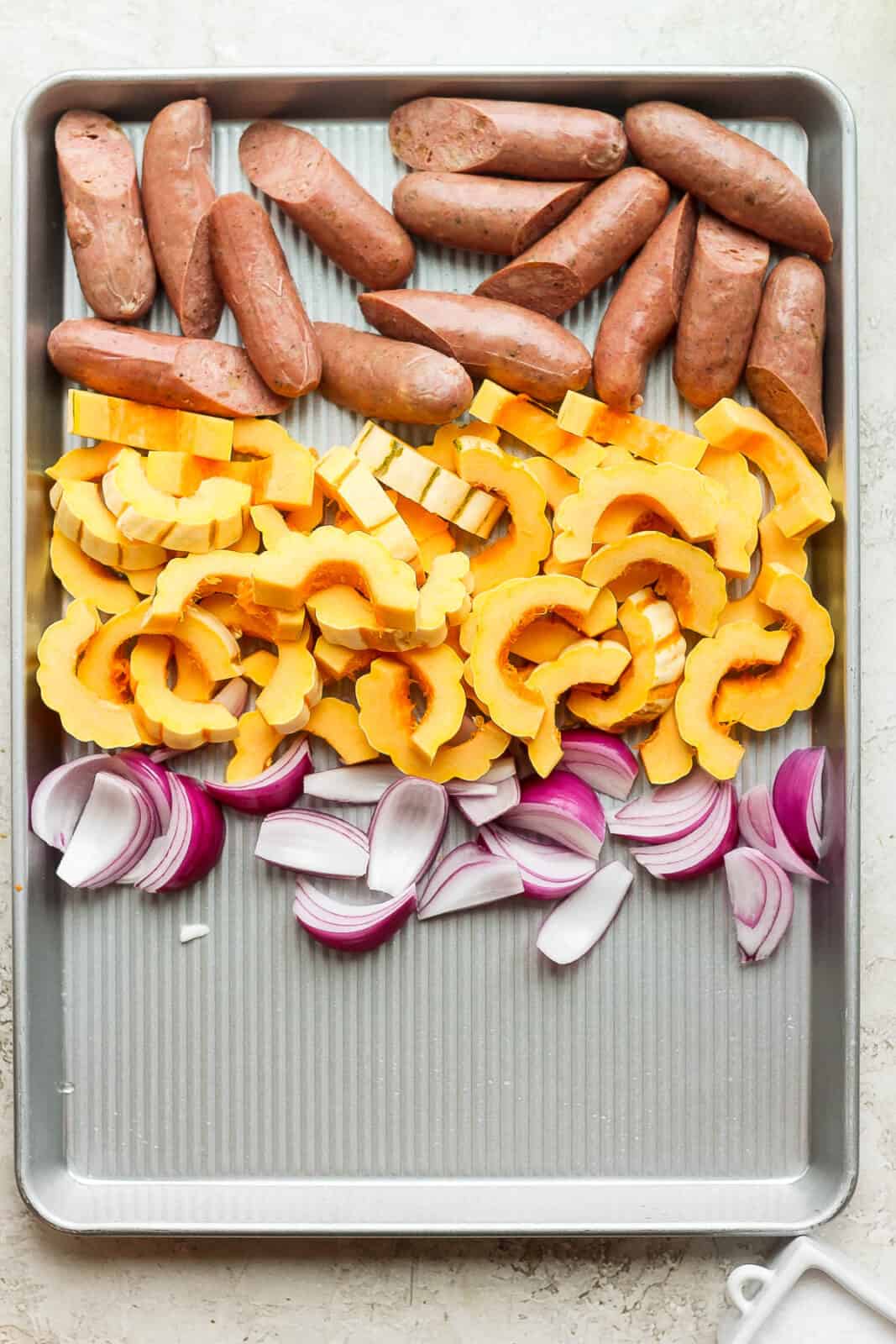 Sausage, squash, and red onions on the sheet pan before baking.