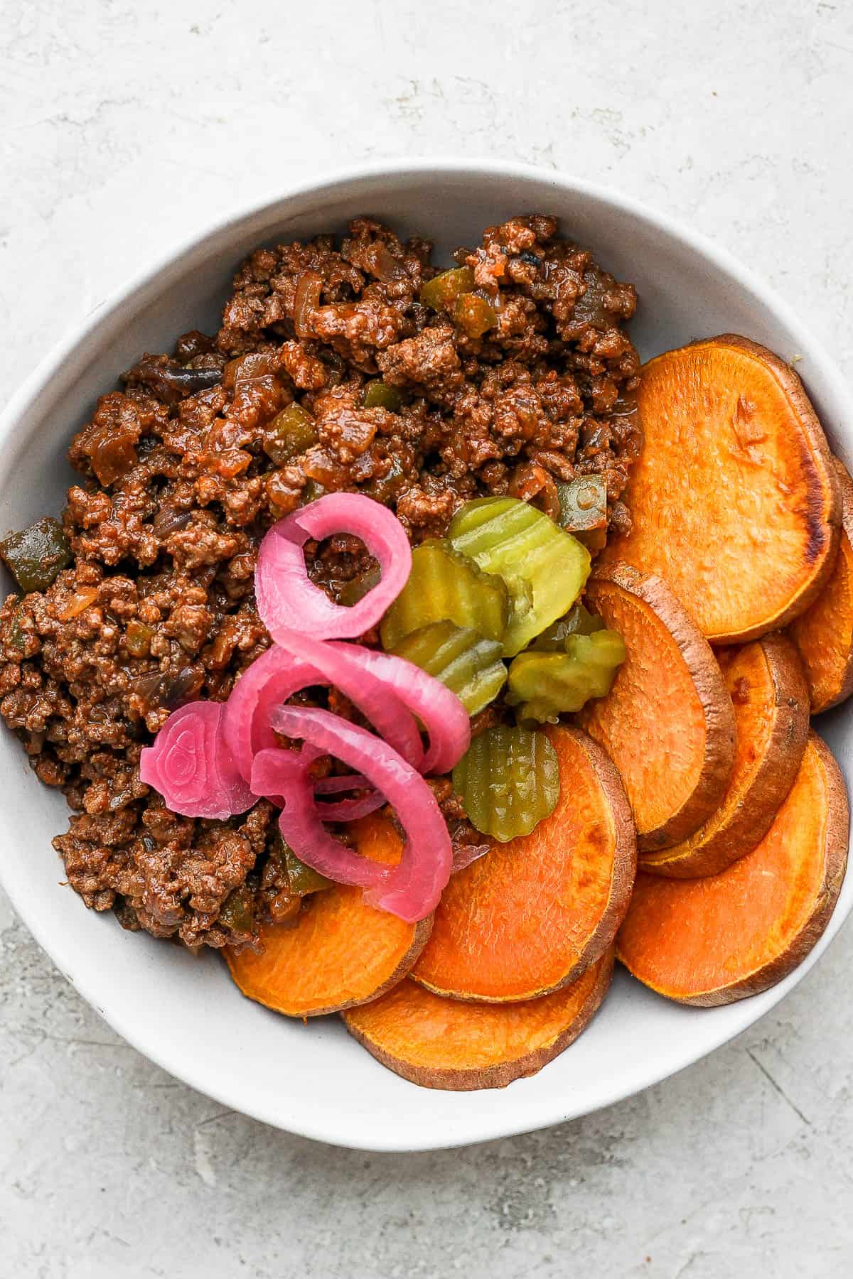 A sloppy joe bowl with pickles and pickled red onion on top.
