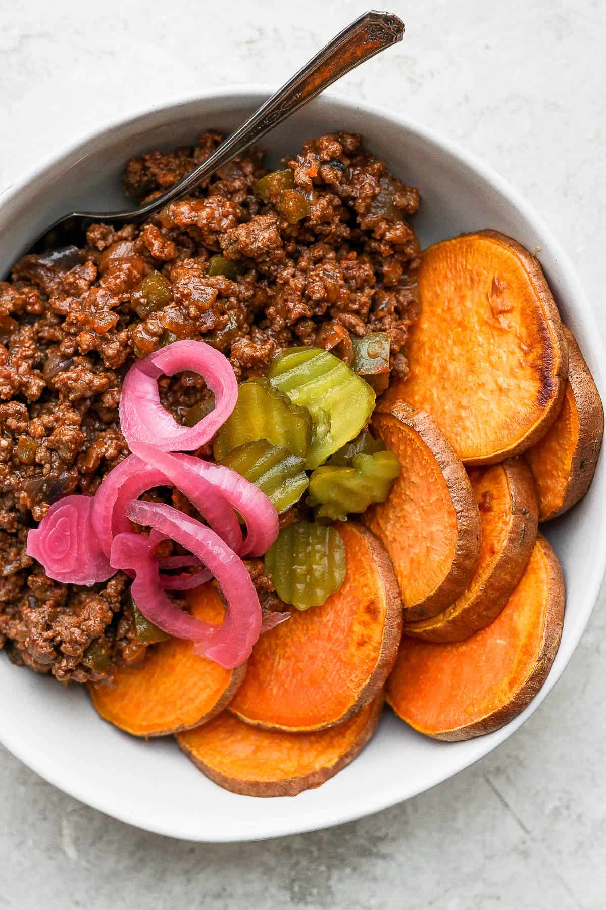 A sloppy joe with pickled onions and burger pickles on top.