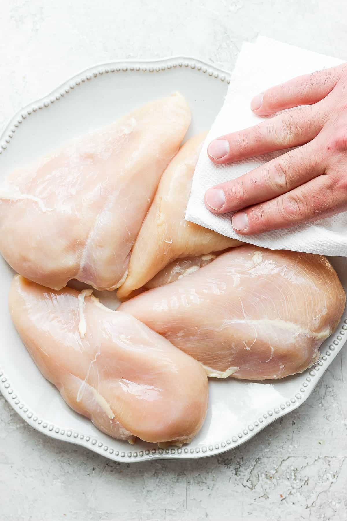 Picture of patting raw chicken breasts dry with clean paper towel. 
