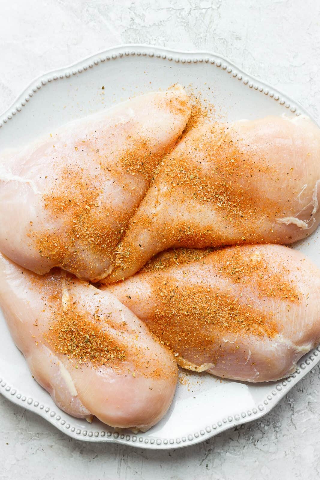 Plate of raw chicken breasts with dry rub on them. 